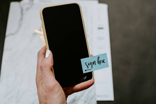 Eine Frauenhand hält ein Handy, auf dessen schwarzem Display ein Post-It mit 