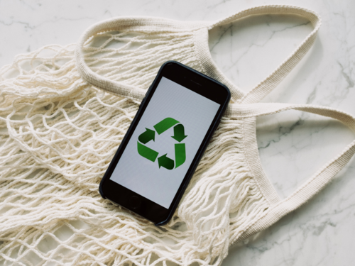 Smartphone mit Recycling-Symbol liegt auf einem wiederverwendbaren Einkaufsnetz aus Baumwolle – Symbol für digitale und nachhaltige Lösungen.